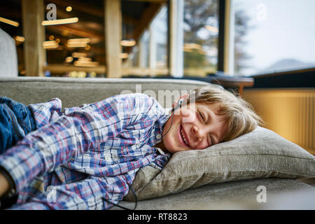 Happy boy lying on couch with earphones Stock Photo