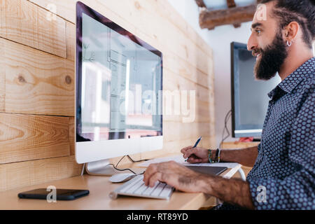 Smiling young man working on floor plan at home using the computer Stock Photo