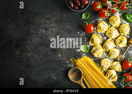 Food background. Italian food background with pasta, ravioli, tomatoes, olives and basil on dark background. Horizontal with copy space. Stock Photo
