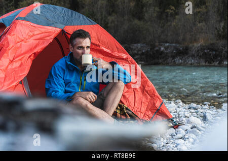Mature man camping at riverside, drinking Stock Photo