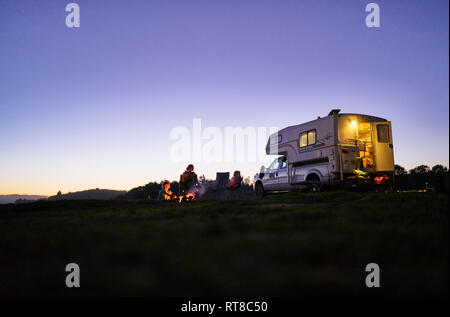 Chile, Talca, Rio Maule, mother with two sons sitting at camp fire at camper Stock Photo