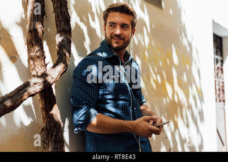 Portrait of smiling man using smartphone and earphones outdoors Stock Photo