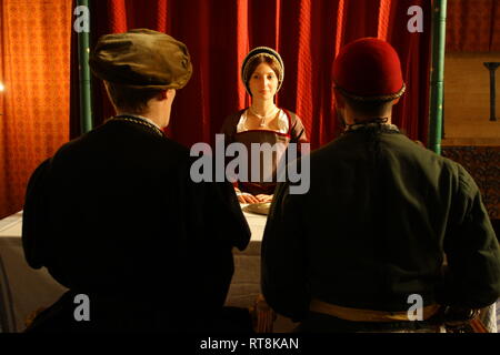 A woman dressed as Anne Boleyn from the Tudor period faces the camera and has a meeting with two Tudor men, with their backs to the camera. Stock Photo