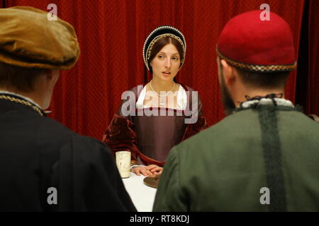 A woman dressed as Anne Boleyn from the Tudor period faces the camera and has a meeting with two Tudor men, with their backs to the camera. Stock Photo