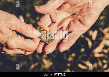 Senior woman hand is holding bitcoin coin giving to senior man hand on green nature background. Business, Finance, Investment and exchanging concepts Stock Photo