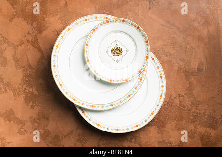 White porcelain ornamental plates of various sizes lie on a textured brown background. Flat layout. Stock Photo
