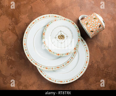 White porcelain plates of various sizes and a circle with an ornament lie on a textured brown background. Flat layout. Stock Photo