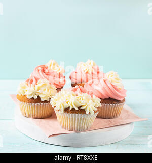 Fresh cupcakes with whipped cream and cream are served on a plate on a soft blue background close-up. Copy space. Stock Photo