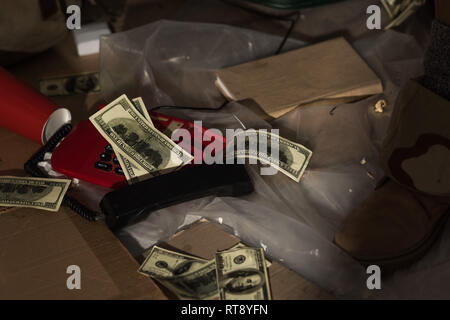 cropped view of male leg in boot near vintage phone, book and money scattered on floor Stock Photo