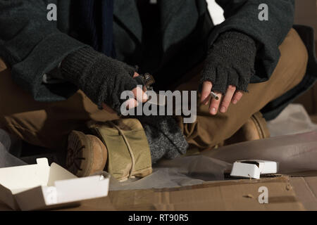 partial view of homeless man in fingerless gloves holding lighter and cigarette Stock Photo