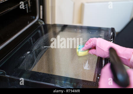 Photo of woman in pink rubber gloves washing oven. Stock Photo