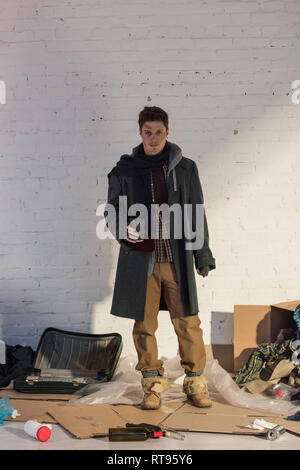 homeless man standing on cardboard and holding disposable cup Stock Photo