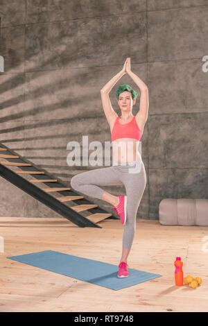 Green-haired woman wearing pink sneakers standing in tree pose Stock Photo