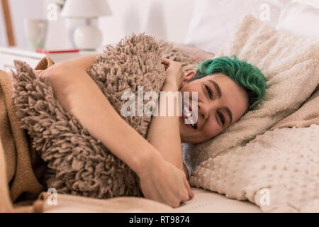 Cheerful woman hugging little fluffy pillow while chilling in bed Stock Photo
