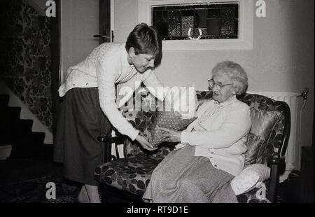 Late 1960s, a pretty teenage girl giving a bunch of flowers to her Grandmother, who is sitting on a small wooden framed sofa, England, UK. Stock Photo