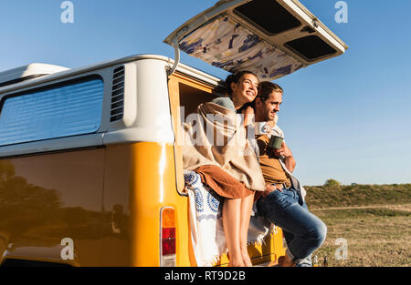 Happy couple doing a road trip with their camper, sitting on their bed, drinking coffee Stock Photo