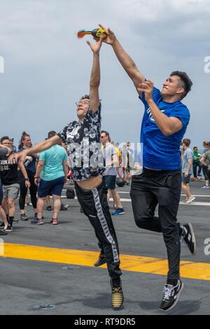 U.S. Navy Engineman Fireman Johnathan Santiago, left, from New York, prevents Engineman 2nd Class Armando Calixtro, from Georgetown, Texas, from catching a ball in a game during a steel beach picnic on the flight deck aboard the aircraft carrier USS John C. Stennis (CVN 74) in the Indian Ocean, Jan. 27, 2019. The John C. Stennis is deployed to the U.S. 7th Fleet area of operations in support of security and stability in the Indo-Pacific region. Stock Photo