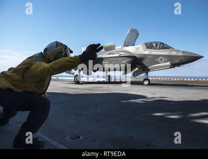 PHILIPPINE SEA (Jan 28, 2019) -- Aviation Boatswain's Mate (Handling) 3rd Class Noel Rulloda, from Chicago, signals the launch of an F-35B Lightning II aircraft belonging to Marine Fighter Attack Squadron 121 from the flight deck of the amphibious assault ship USS Wasp (LHD 1). Wasp, flagship of Wasp Amphibious Ready Group, with embarked 31st Marine Expeditionary Unit, is operating in the Indo-Pacific region to enhance interoperability with partners and serve as a ready-response force for any type of contingency. Stock Photo