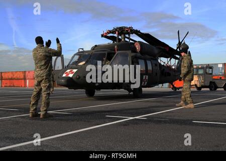 Soldiers with 601st Aviation Support Battalion, 1st Combat Aviation Brigade, 1st Infantry Division ground guides a UH-60 Black Hawk helicopter during port operations Jan. 29 at Zeebrugge, Belgium. 1st CAB is deployed to Europe for a nine-month rotation and stands ready to provide world-class support to Atlantic Resolve, a key opportunity to train with U.S.Allies and partners, and demonstrate U.S. commitment to our collective security. Stock Photo