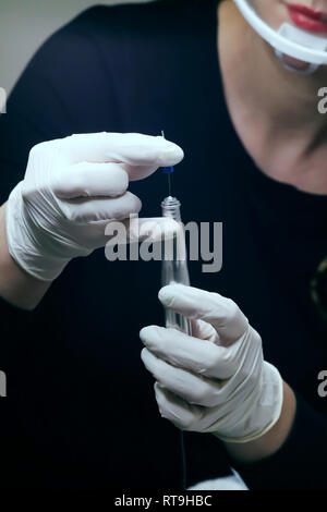 Professional beautician in black with white gloves putting needle on  special tattoo device preparing for permanent make-up in beauty studio, close up Stock Photo