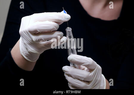 Professional beautician in black with white gloves putting needle on  special tattoo device preparing for permanent make-up in beauty studio, close up Stock Photo