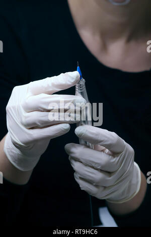 Professional beautician in black with white gloves putting needle on  special tattoo device preparing for permanent make-up in beauty studio, close up Stock Photo