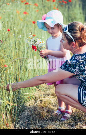 Mother and her little daughter in the field of wild flowers. Little girl picking the spring flowers for her mom for Mother's Day in the meadow. Nature Stock Photo