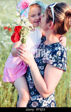 Mother and her little daughter in the field of wild flowers. Little girl picking the spring flowers for her mom for Mother's Day in the meadow. Girl h Stock Photo