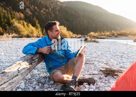 Mature man camping at riverside, using tablet Stock Photo
