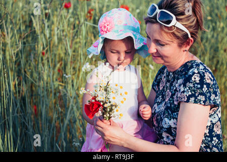 Mother and her little daughter in the field of wild flowers. Little girl picking the spring flowers for her mom for Mother's Day in the meadow. Nature Stock Photo