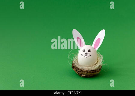 Busket with Easter bunny made from eggs and paper ears on green pastel background. Creative idea. Art food concept. Stock Photo