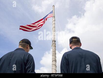 SINGAPORE (Jan. 31, 2019) Aviation Support Equipment Technician 2nd Class Salam Sabah, from Detroit, left, and Aviation Boatswain’s Mate (Fuel) 3rd Class Dylan Wilson, from Hawkins, Texas, prepare to lower the American flag aboard the San Antonio-class amphibious transport dock ship USS Anchorage (LPD 23) while on a deployment of the Essex Amphibious Ready Group (ARG) and 13th Marine Expeditionary Unit (MEU). The Essex ARG/13th MEU is a capable and lethal Navy-Marine Corps team deployed to the 7th fleet area of operations to support regional stability, reassure partners and allies and maintain Stock Photo