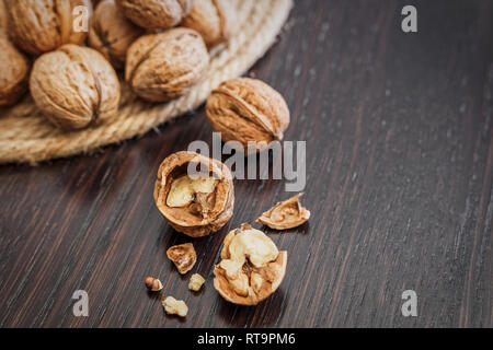 Close-up view of walnut kernels and whole walnuts on a dark wooden table, space for text. Healthy food concept. Stock Photo