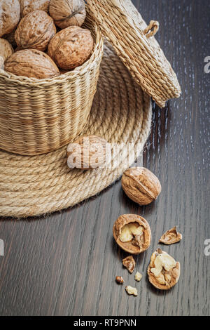 Whole walnuts in basket and walnut kernels on a dark wooden table, space for text. Healthy food concept. Stock Photo