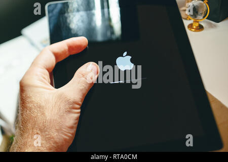 PARIS, FRANCE - SEP 12, 2014: Male hand holding Apple Computers logotype on the retina screen display of the latest iPad tablet  displaying progress update loading bar Stock Photo