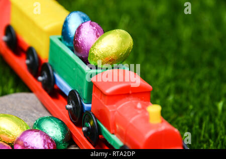 Closeup of Easter eggs toy plastic train traveling on railway on lawn. Concept of fun, play, Easter, play, plastic and transport Stock Photo