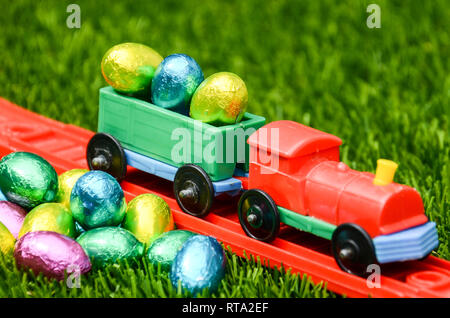 Bright colourful fun toy train with load of Easter Eggs and pile on Easter Eggs on grass. Concept Easter, holidays, play and childhood Stock Photo
