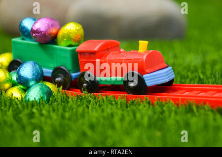 Plastic toy train with load of Easter Eggs in outdoors lawn scene. Colour bright concept of Easter, holidays, travel and childhood play. Stock Photo