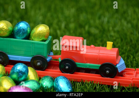 Colourful plastic toy train transport bright coloured easter eggs on railway track on grass. Concept of childhood, play, travel and easter holidays. Stock Photo