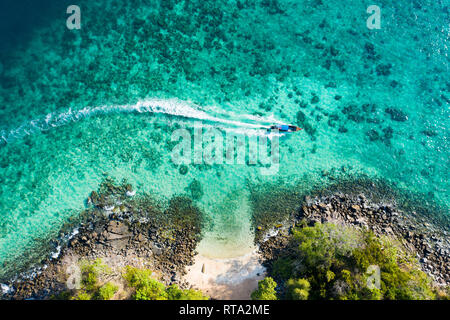 View from above, aerial view of a traditional long-tail boat sailing near a stunning barrier reef with a beautiful small beach. Stock Photo