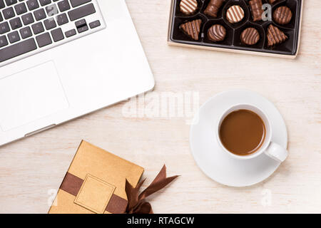 Glass of chocolate milk and variety chocolates  on table with gift box and laptop. Stock Photo
