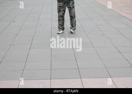 Men feet in old white sneakers and camouflage trousers on pavement on the street. Stock Photo