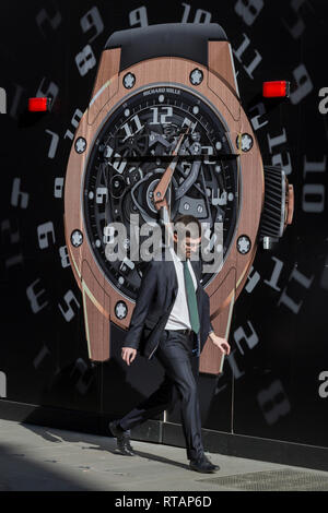 A businessman walks past a construction hoarding of a watch