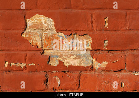 Old brick wall behind a layer of crumbling painted red plaster, background or texture. Stock Photo