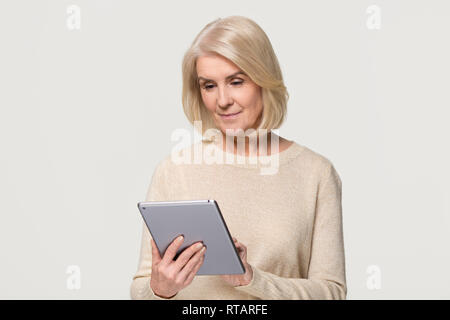 Mature woman using digital tablet isolated on grey studio background Stock Photo