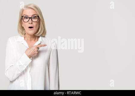 Surprised mature businesswoman pointing finger at copyspace isolated on background Stock Photo