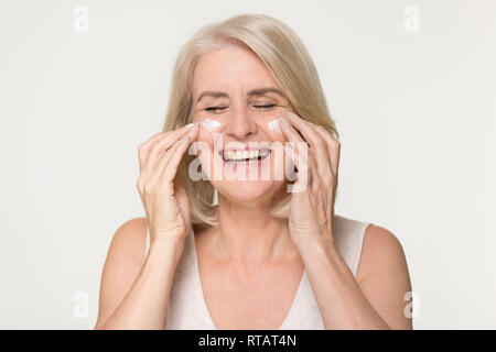 Happy old woman apply anti aging cream isolated on background Stock Photo