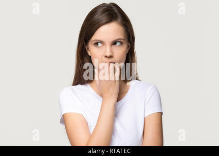 Nervous insecure young woman biting nails isolated on grey background Stock Photo