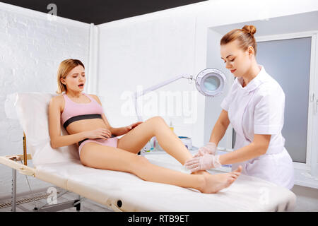 Woman with bob cut feeling painful while having leg depilation Stock Photo