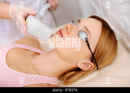 Woman wearing protective glasses having photo depilation of chin Stock Photo